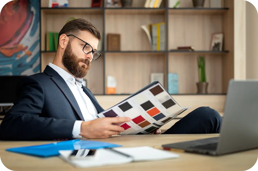 Man in a blazer reading a colour swatch catalogue at his desk