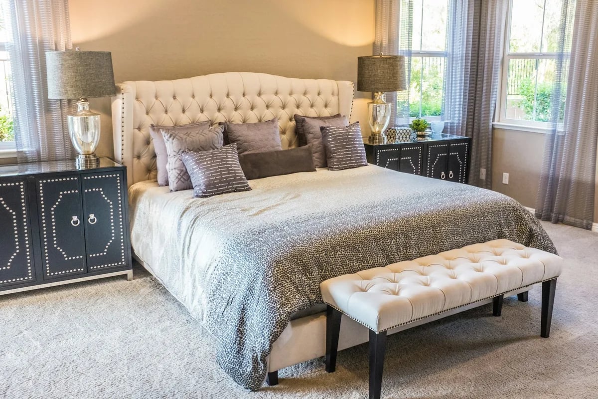 Made bed with a tufted headboard and grey bedding in a staged bedroom