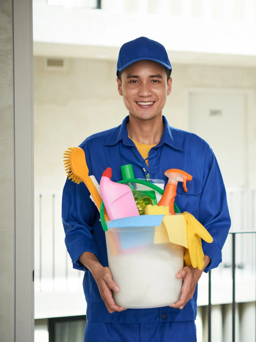 Uniformed cleaning professional holding a caddy of cleaning supplies